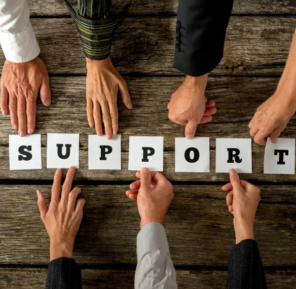 Seven business people holding white cards with letters to assemble the word SUPPORT on textured wooden desk. Conceptual of teamwork, cooperation and customer service.